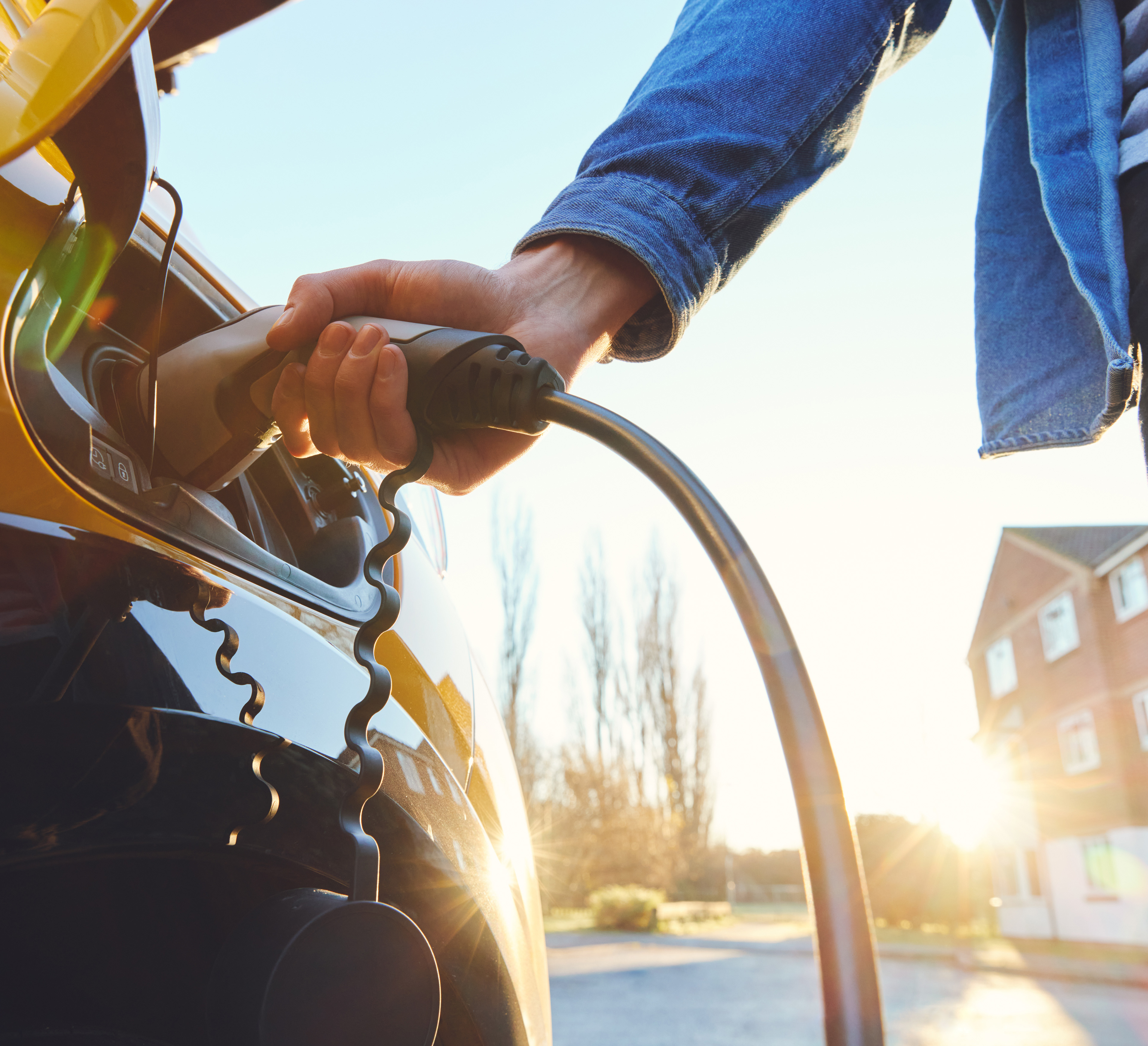 La mano di un uomo ricarica un veicolo elettrico tenendo un bocchettone attaccato alla presa dell'auto.